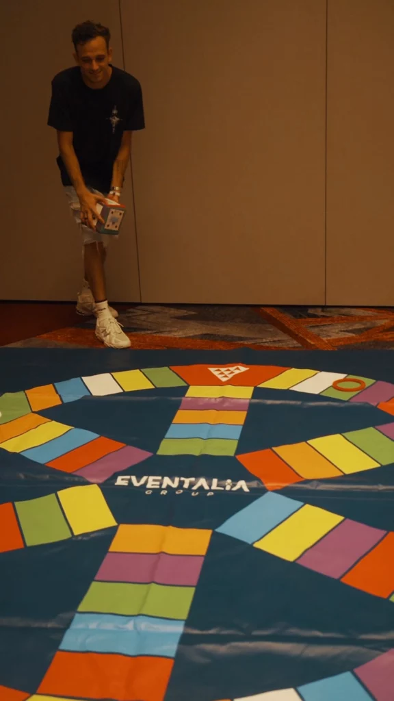 Participante lanzando un dado en un tablero de Trivial gigante durante una jornada de team building para empresas en Canarias.